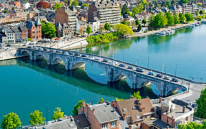 Pont en pierre traversant une rivière avec des voitures, entouré de bâtiments en briques et d'arbres verts sous un ciel dégagé.