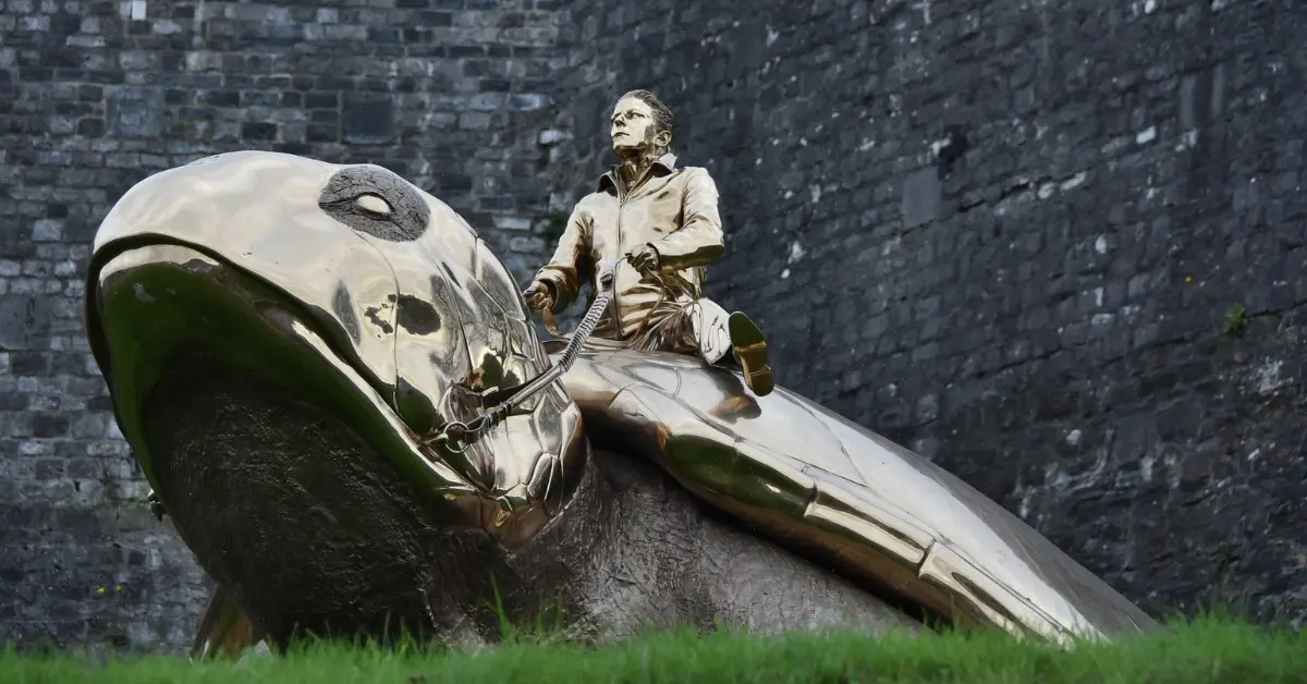 Statue dorée représentant un homme assis sur une immense tortue, devant un mur en pierre grise.