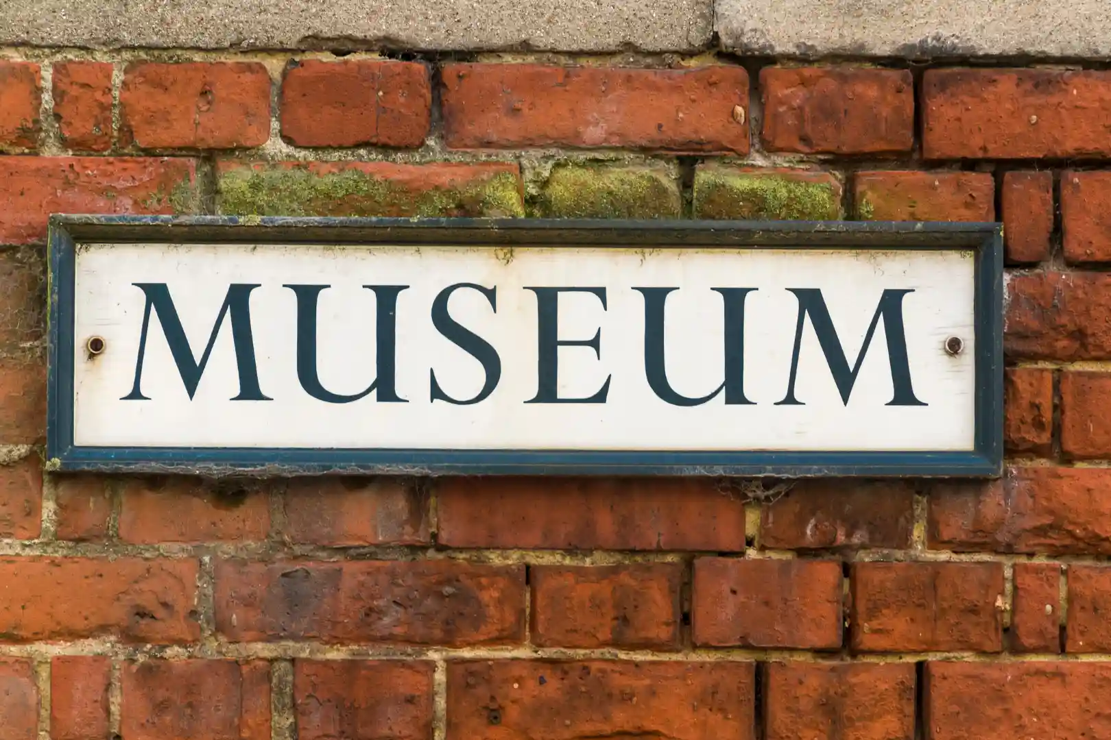 Plaque blanche avec le mot "Museum" en lettres noires, fixée sur un mur de briques rouges.