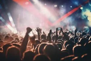 Foule de personnes levant les bras et prenant des photos avec leurs téléphones lors d'un concert, éclairée par des lumières colorées.
