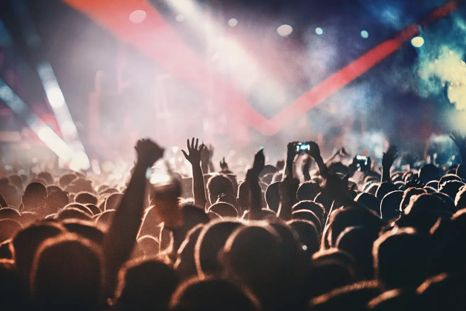 Foule de personnes levant les bras et prenant des photos avec leurs téléphones lors d'un concert, éclairée par des lumières colorées.