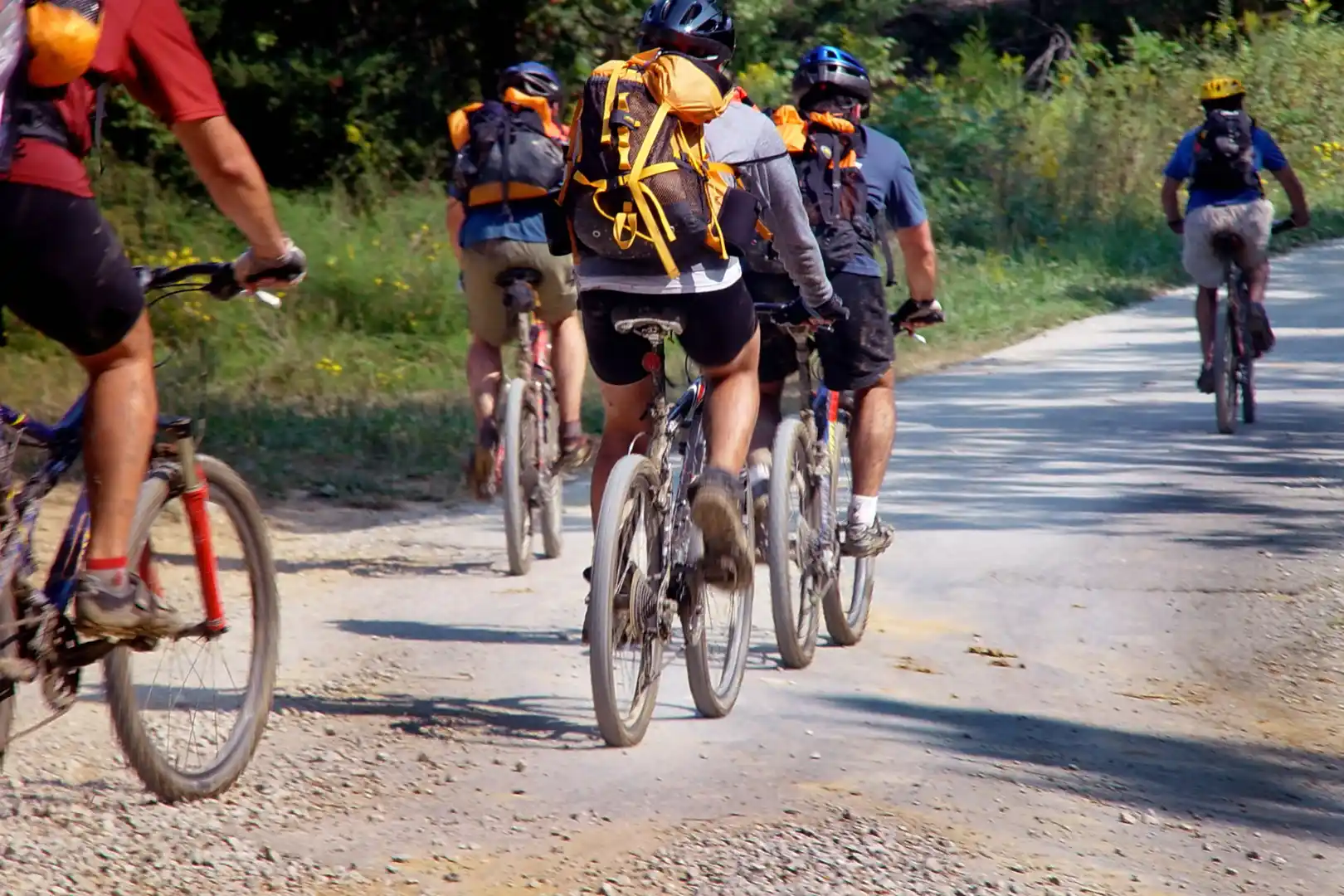 Cyclistes en tenue de sport avec sacs à dos pédalent sur un chemin de terre entouré de verdure.