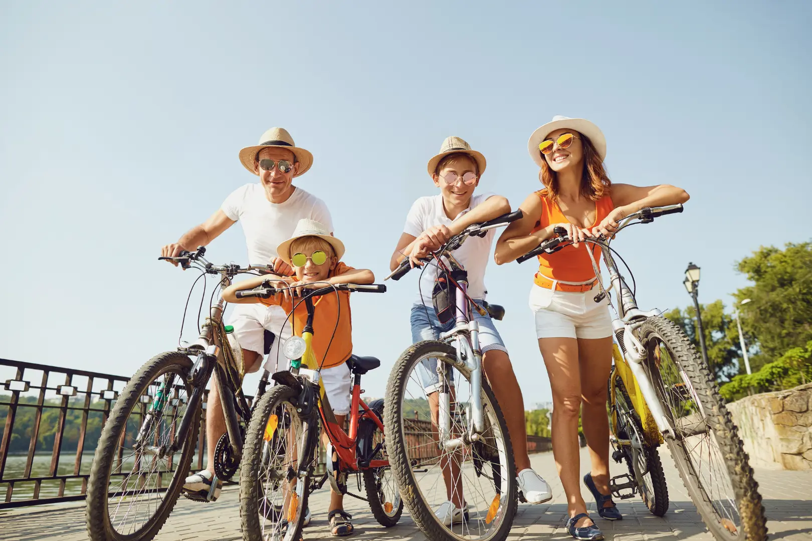 Quatre personnes en tenue estivale et chapeaux de paille posent avec des vélos sur un pont ensoleillé.