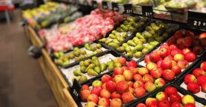 Pommes rouges et vertes, poires vertes et tomates disposées dans des bacs en plastique sur un présentoir de supermarché.