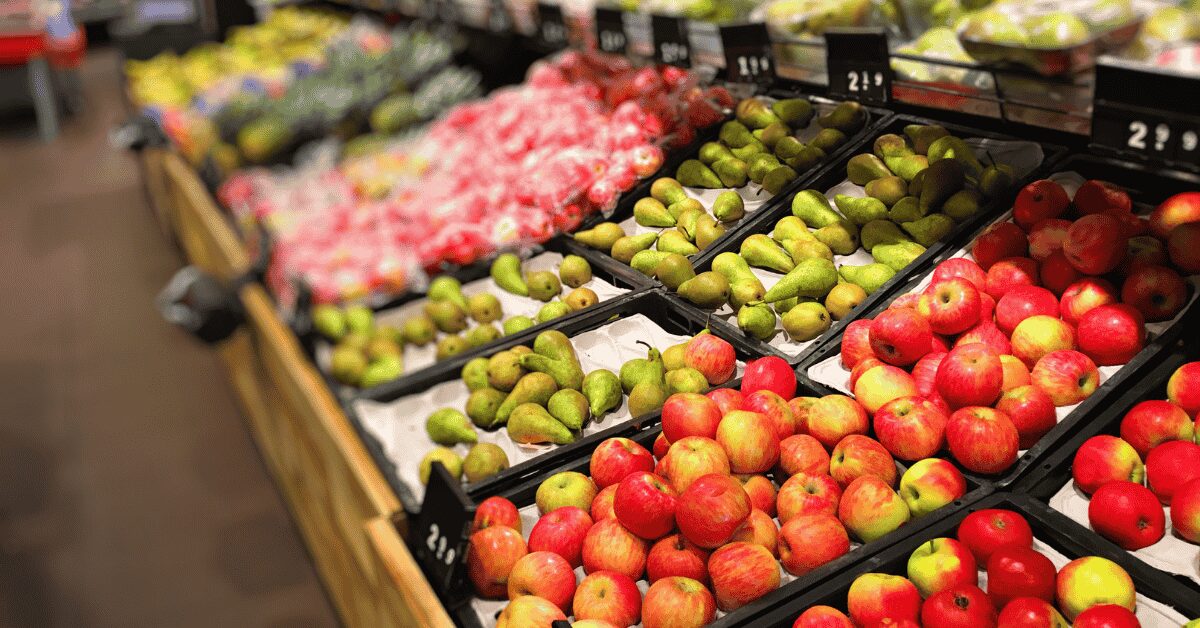 Pommes rouges et vertes, poires vertes et tomates disposées dans des bacs en plastique sur un présentoir de supermarché.