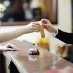 Deux personnes échangent une clé dorée au-dessus d'un comptoir en bois, avec une cloche d'hôtel argentée en arrière-plan.