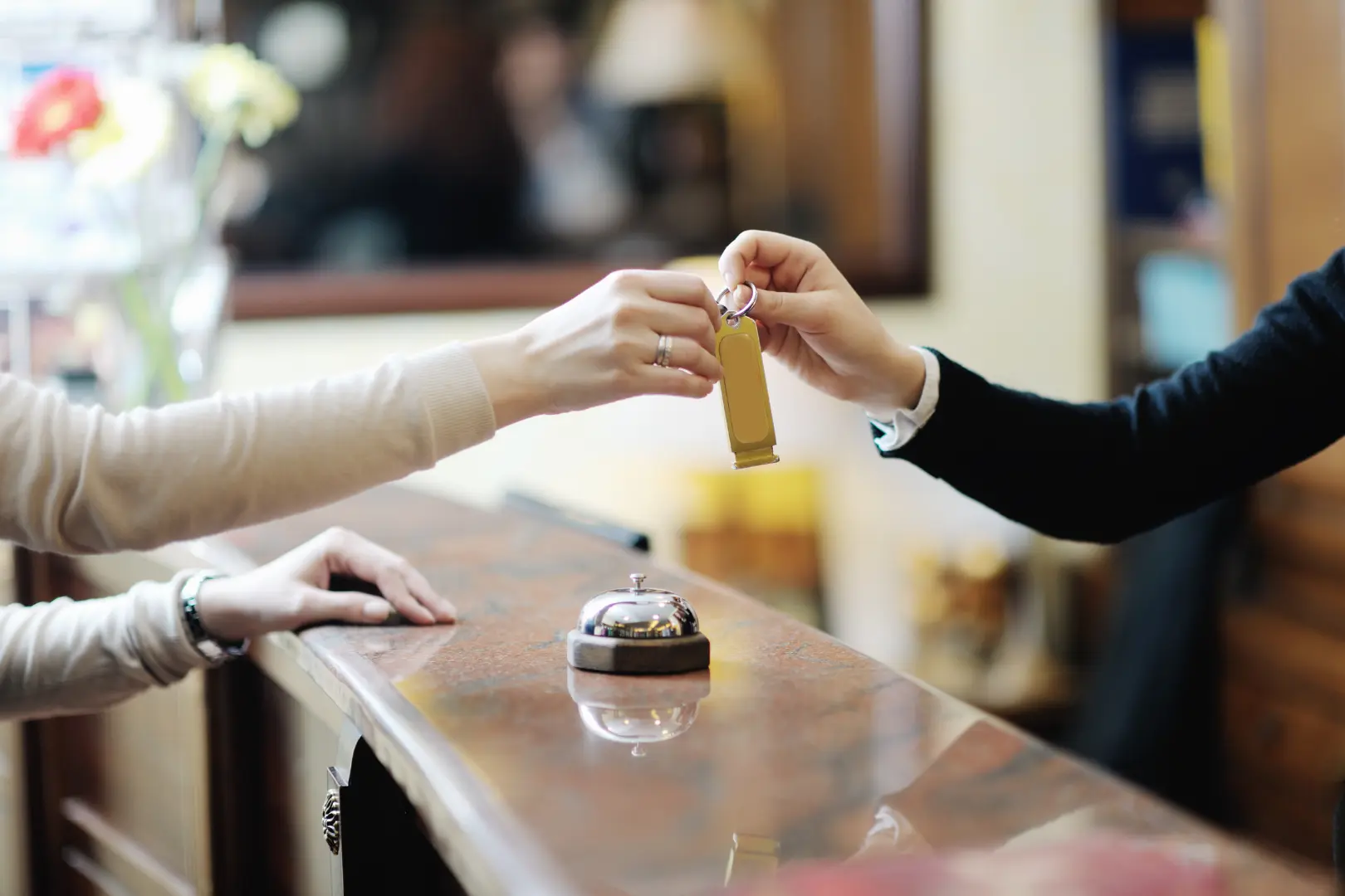 Deux personnes échangent une clé dorée au-dessus d'un comptoir en bois, avec une cloche d'hôtel argentée en arrière-plan.
