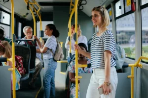 Des passagers se tiennent debout et assis dans un bus, entourés de barres de maintien jaunes, portant des vêtements décontractés.