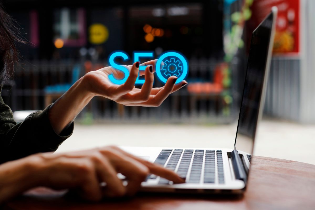 Mains de femme devant un ordinateur portable avec le mot "SEO" dans sa main gauche