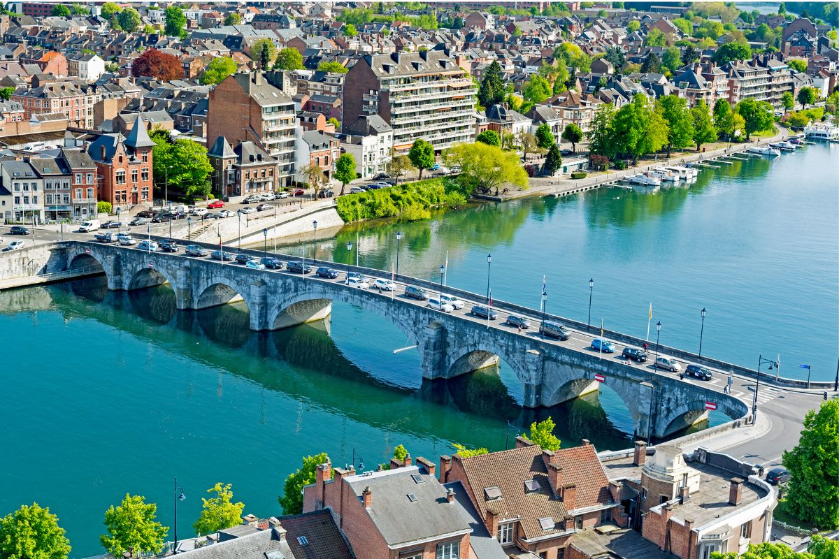 Vue aérienne d'un pont en pierre traversant une rivière, entouré de bâtiments en briques et d'arbres verts à Namur.